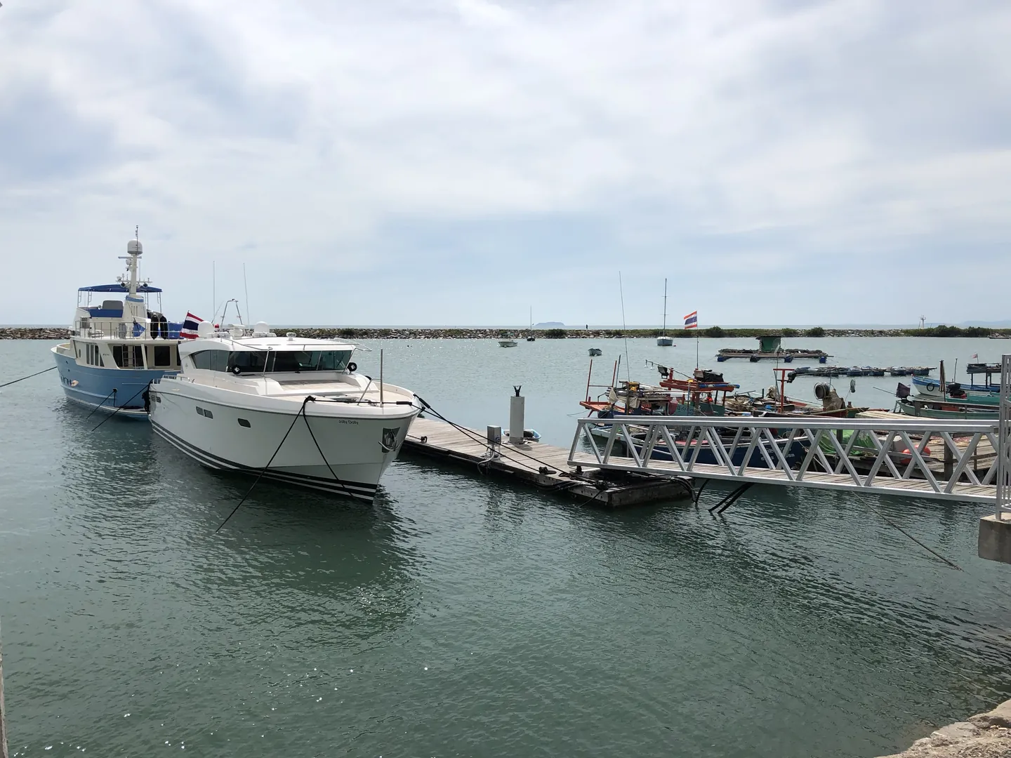 White motor boats and fishing boats moored at a small pier inside a breakwater on an overcast day