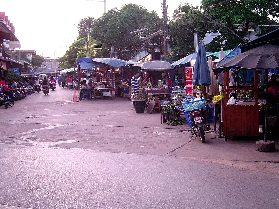 Evening market in Klaeng with covered stalls, umbrellas and motorbikes along the street